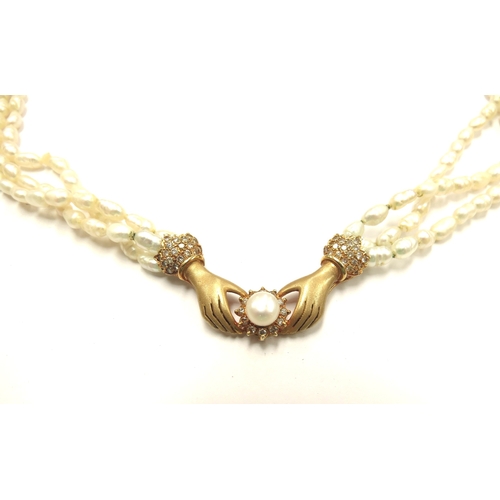 6106 - A triple strand freshwater pearl necklace with hands to centre clasping a pearl framed by diamonds, ... 