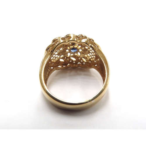 6011 - A gold diamond and sapphire ring in ornate scroll and pierced mount, the central sapphire surrounded... 