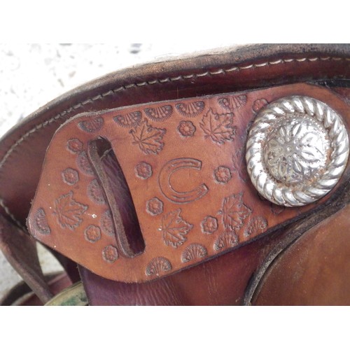 1049 - A tan leather Western saddle with leather stirrups, tooled botanical decoration and sheep’s wool lin... 