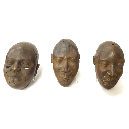 6299 - Three Benin bronze masks of human face form, holes to casting. 18.5cm, 19.5cm and 20.5cm tall