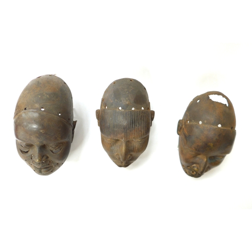 6299 - Three Benin bronze masks of human face form, holes to casting. 18.5cm, 19.5cm and 20.5cm tall