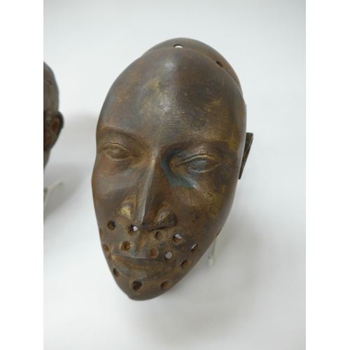 6299 - Three Benin bronze masks of human face form, holes to casting. 18.5cm, 19.5cm and 20.5cm tall