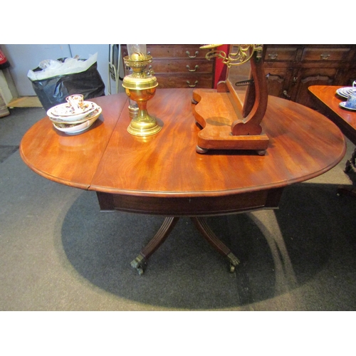 1097 - A mahogany drop-leaf oval dining table, paw feet on brass castors, 72cm tall x 140cm wide x 104cm wi... 