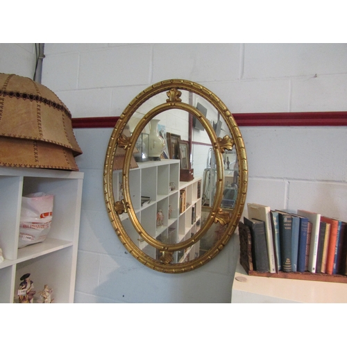 1470 - A Sheraton style gilt wall mirror, oval form with foliate mounts, 92cm height, 72cm width