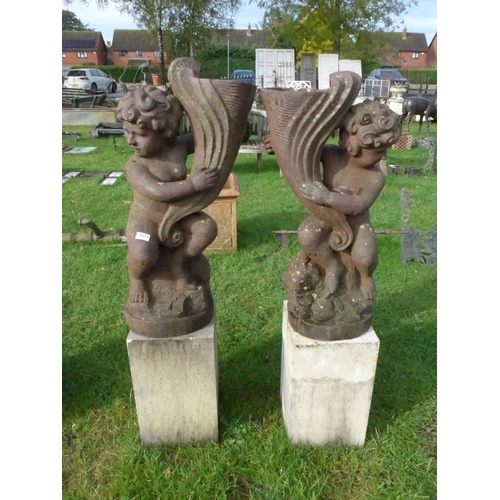 8323 - Two cast iron statues of cherubs with shells standing on associated sandstone square plinths, total ... 