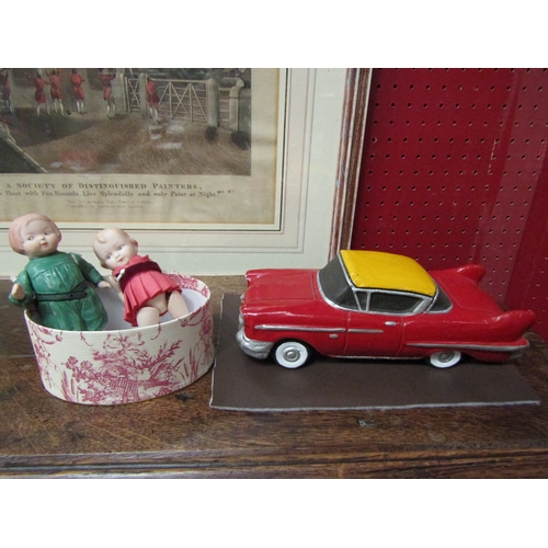 4116 - A painted terracotta car together with two bisque dolls with articulated arms