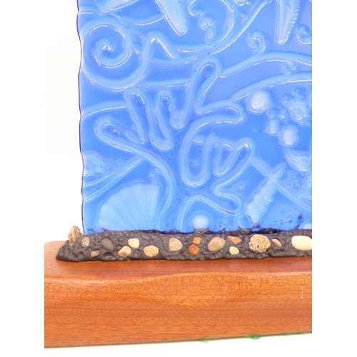 7263 - A large contemporary blue glass relief panel with sea urchin decoration, set on a wooden base. 35cm ... 