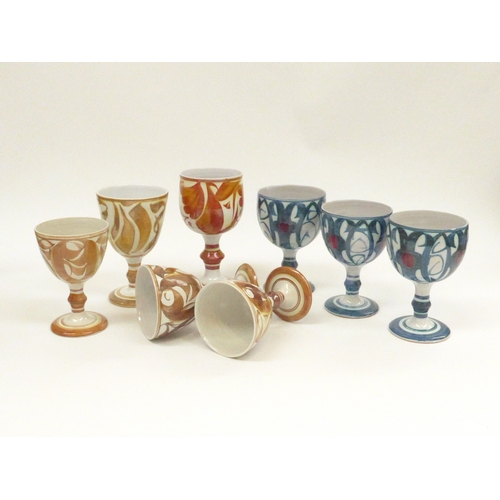 7130 - A collection of eight Aldermaston Pottery goblets in various designs, decorators marks to bases, tal... 