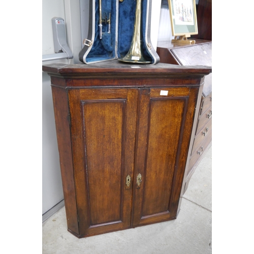 2164 - A George III oak corner cabinet, the two doors opening to reveal painted shelving