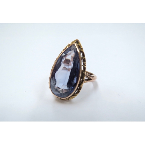 9055 - A gold ring set with a pear shaped blue stone, 2cm long, in a pierced mount on later unmarked gold s... 