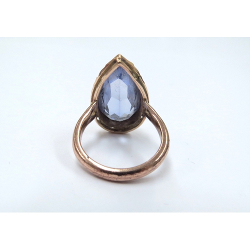 9055 - A gold ring set with a pear shaped blue stone, 2cm long, in a pierced mount on later unmarked gold s... 