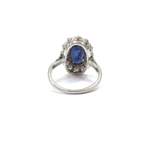 9150 - A platinum sapphire and diamond cluster ring the central oval sapphire 11mm x 7mm framed by fourteen... 