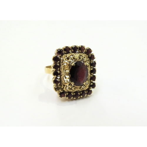 9342 - A gold ring with central garnet in an ornate scroll pierced frame surrounded by smaller garnets (one... 