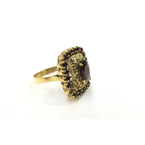 9342 - A gold ring with central garnet in an ornate scroll pierced frame surrounded by smaller garnets (one... 