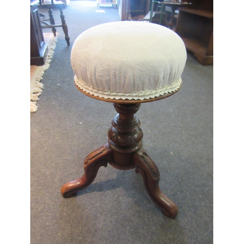 1074 - A mahogany cream upholstered swivel piano stool on tripod feet