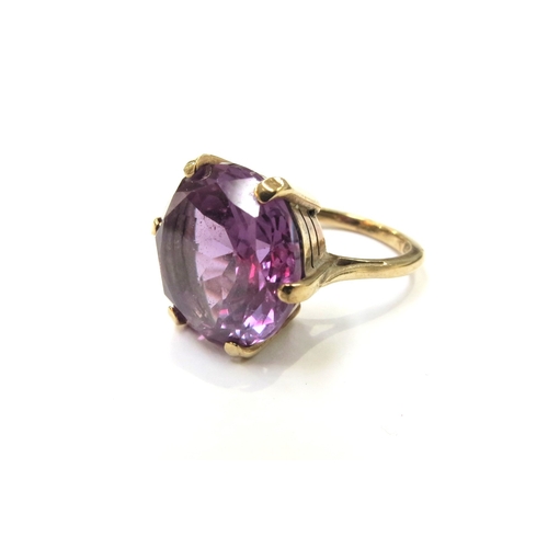 6122 - A gold ring set with a large amethyst coloured stone, possibly synthetic violet sapphire, shank stam... 