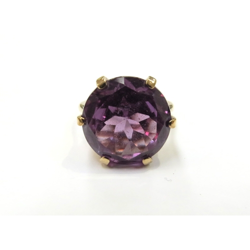 6122 - A gold ring set with a large amethyst coloured stone, possibly synthetic violet sapphire, shank stam... 