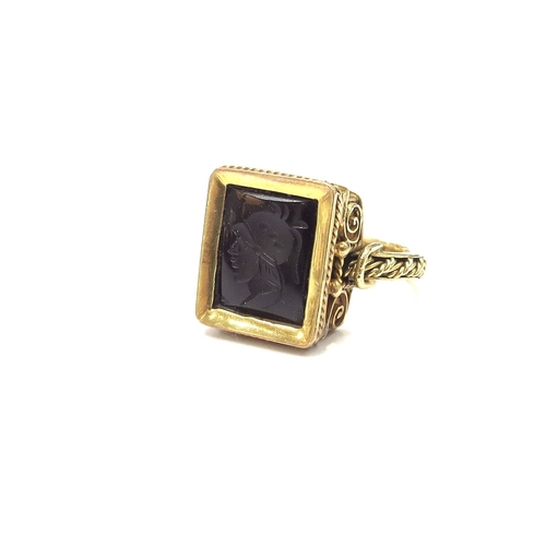 6163 - An unmarked gold ring with an intaglio depicting a bust of a Roman soldier, ornate scroll frame. Siz... 