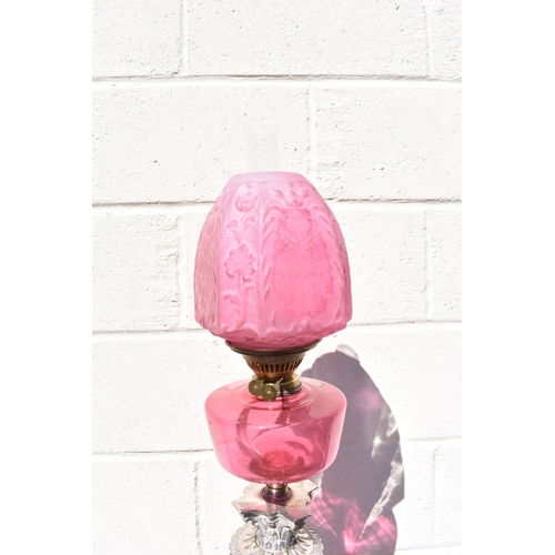 1011 - A late 19th Century French cranberry glass oil lamp with Art Nouveau moulded shade, above cranberry ... 