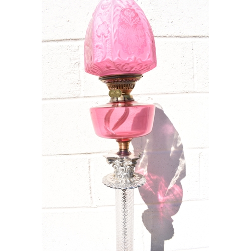 1011 - A late 19th Century French cranberry glass oil lamp with Art Nouveau moulded shade, above cranberry ... 