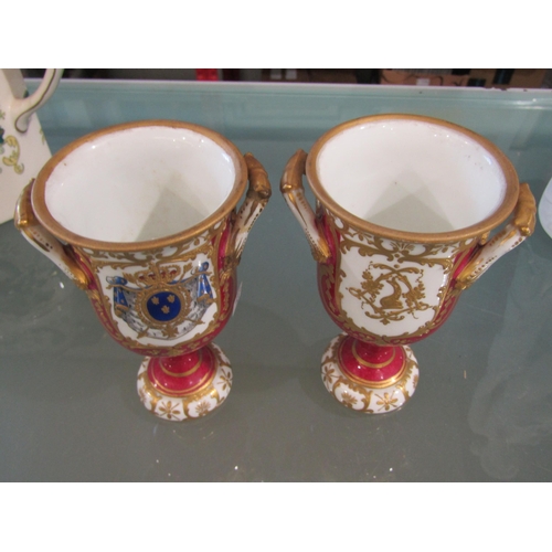 1046 - A pair of Continental porcelain urns with armorial decoration, 13cm tall, handle restored to one
