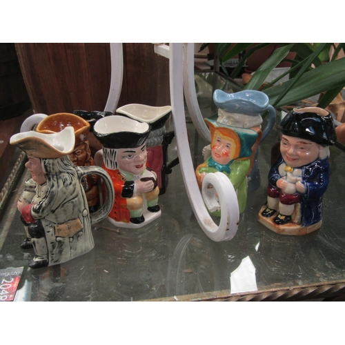 2044 - A quantity of plaster maidens heads in glass vase and nine Toby style jugs