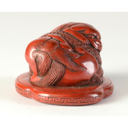 9045 - A red lacquered netsuke in the form of two shishi wrapped around a ball, flat base

3.8cm wide x 3.4... 