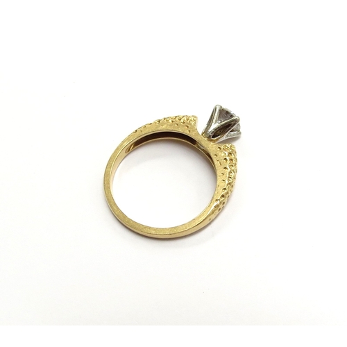 6058 - A diamond solitaire ring in four claw mount within a textured shank, 18ct. Size M/N, 4g