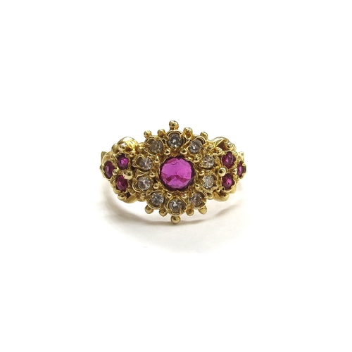 6040 - An 18ct gold ruby and diamond cluster ring, the central round ruby framed by diamonds with three rub... 