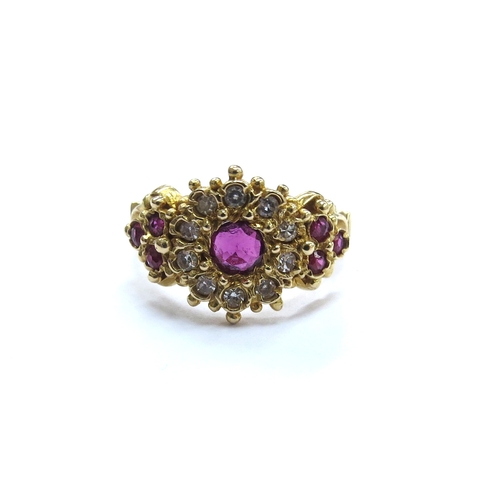 6040 - An 18ct gold ruby and diamond cluster ring, the central round ruby framed by diamonds with three rub... 