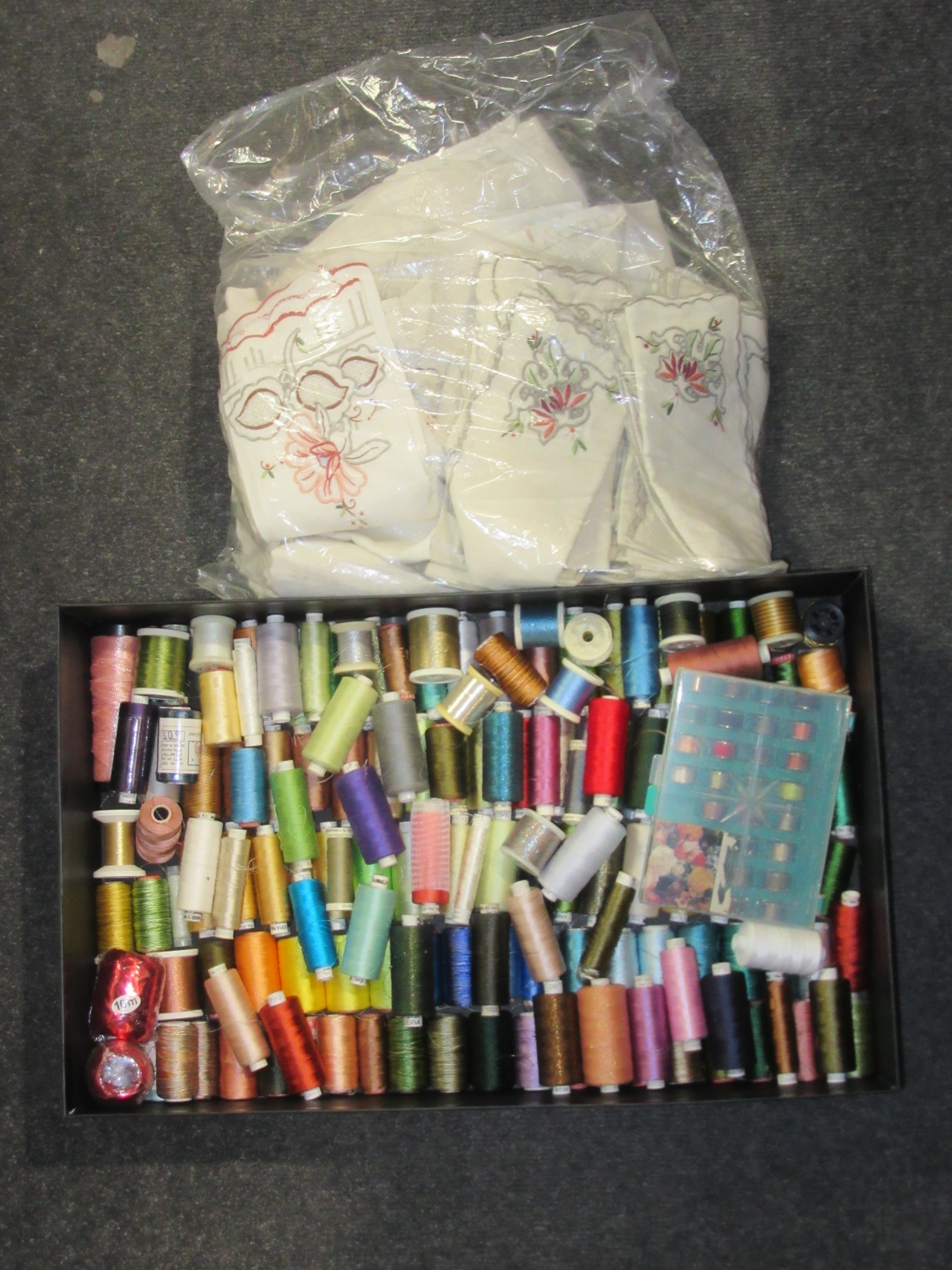 A box containing various sewing threads and a bag of table linens