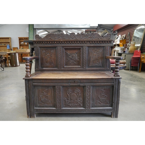 2001 - An 18th Century carved oak settle, three heraldic panels to back and front, rising seat, outswept ar... 
