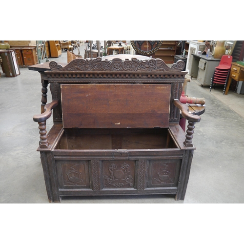 2001 - An 18th Century carved oak settle, three heraldic panels to back and front, rising seat, outswept ar... 