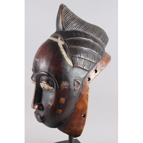 152 - A West African carved hardwood tribal mask, on ebonised stand, 13 1/4