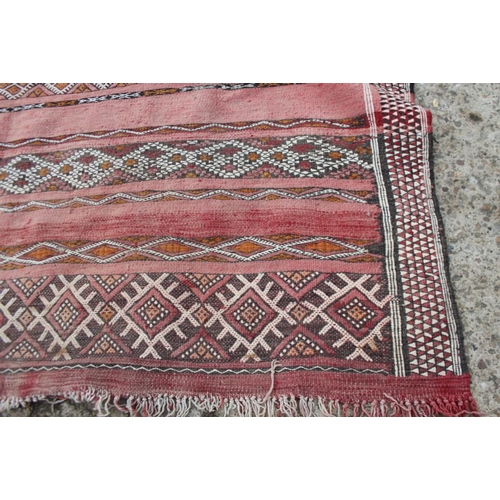 737 - A Moroccan tribal rug decorated bands of geometric ornament on a red ground, 106