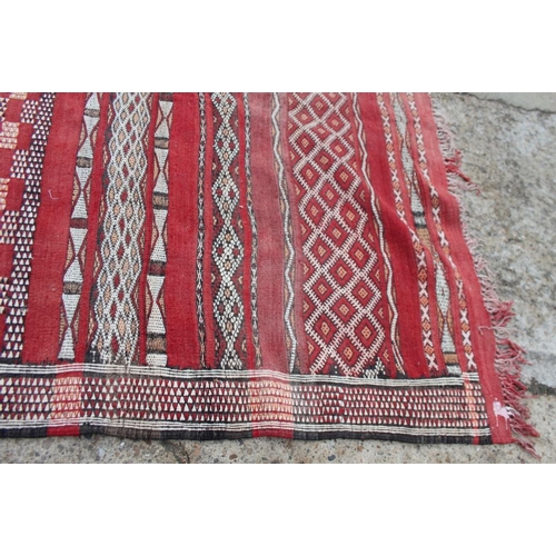 737 - A Moroccan tribal rug decorated bands of geometric ornament on a red ground, 106