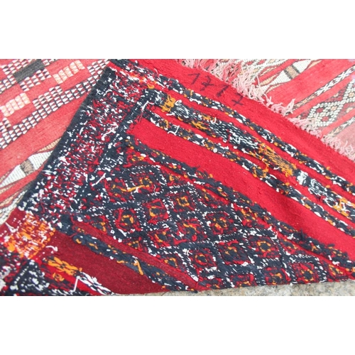 737 - A Moroccan tribal rug decorated bands of geometric ornament on a red ground, 106