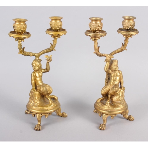 129 - A pair of gilt metal candelabra with fauns holding a bird, on claw supports 9 1/2