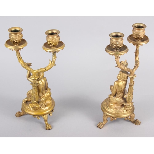 129 - A pair of gilt metal candelabra with fauns holding a bird, on claw supports 9 1/2