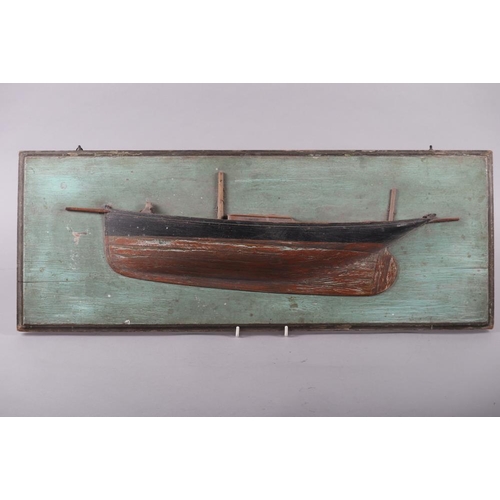 134 - A carved and painted softwood scale model half hull of a yacht, on green painted backboard, 26