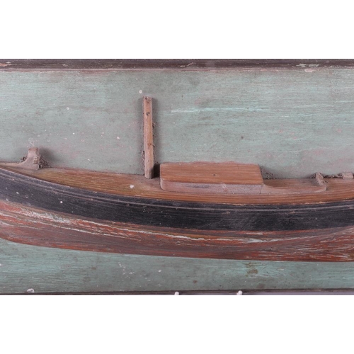 134 - A carved and painted softwood scale model half hull of a yacht, on green painted backboard, 26