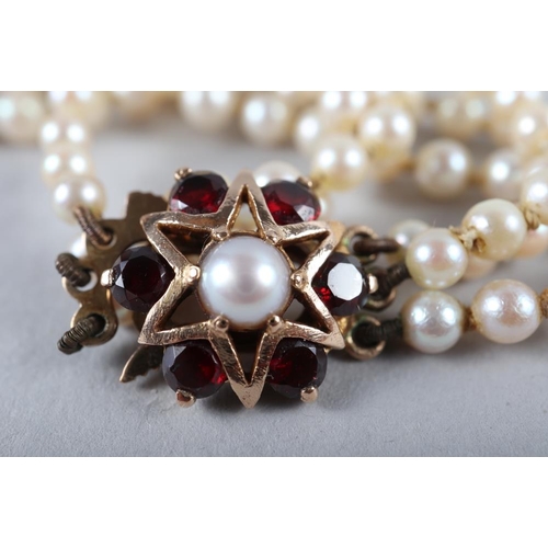 229 - A Mikimoto cultured pearl three-strand necklace with 9ct gold and garnet set star clasp, in case. 
T... 