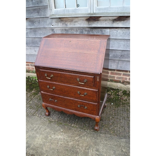 413 - An oak bureau with three graduated drawers, on claw and ball supports, 28 1/2