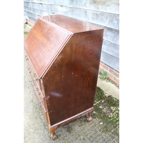 413 - An oak bureau with three graduated drawers, on claw and ball supports, 28 1/2