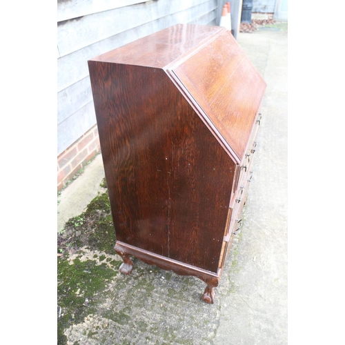 413 - An oak bureau with three graduated drawers, on claw and ball supports, 28 1/2