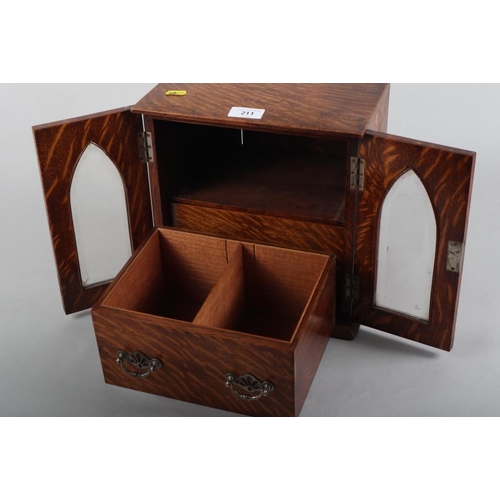 211 - An oak cigar box with  two cedar lined drawers enclosed Gothic style glazed doors and two carrying h... 