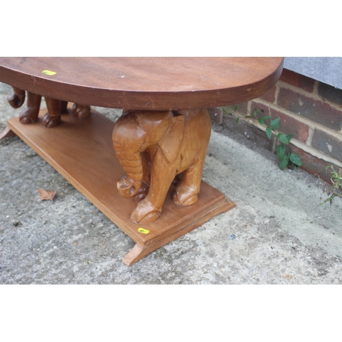 590 - A 1960s oval teak low coffee table, on elephant supports, 42