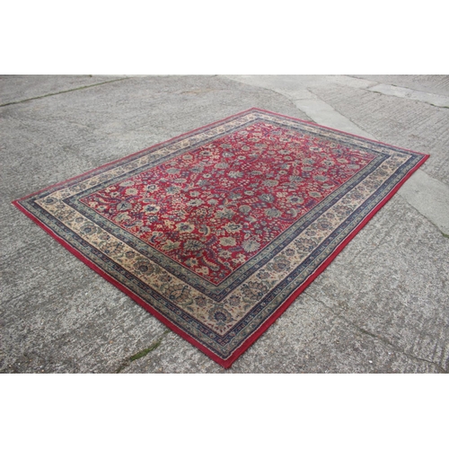 669 - A Persian style machine woven rug with floral designs on a red ground in shades of natural, blue and... 