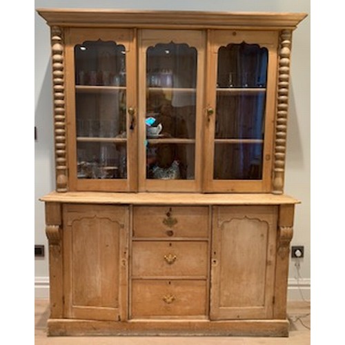 744 - A stripped pine bookcase, the upper section enclosed three shaped panel glazed doors over three cent... 