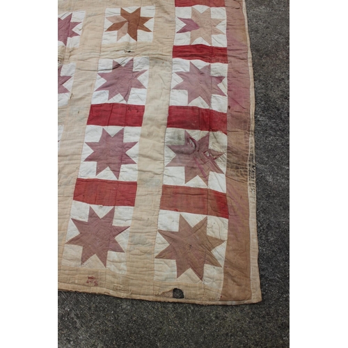 193 - An early 20th century quilt with thirty central star-shaped guls in shades of red and cream, 74 1/2